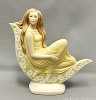 Side view of the porcelain figurine showing the female figure seated on a crescent decorated with daisies.