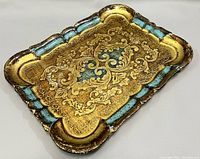 Angled view of the tray showing embossed gold floral scroll design with turquoise and black accents on scalloped edges.