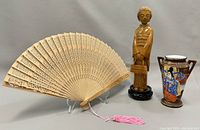 Photo showing carved wooden fan, wooden statue figure, and decorated ceramic vase together for context and detail.