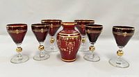 Six red Bohemian style wine glasses arranged in two rows to show the gold trim and different sizes, highlighting the intricate gold decoration near the rims and the gold spheres in clear stems.