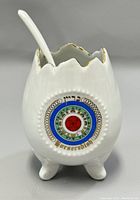 Front view of white ceramic horseradish dish shaped like cracked egg with gold edging and colorful circular motif.