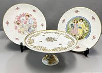 Porcelaine De France hand painted cake stand with gold floral patterns flanked by two Royal Doulton collectible plates with Victorian children and floral designs.