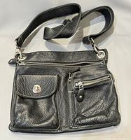 Front view of black leather Roots shoulder bag showing two front pockets - one flap button pocket, one zipper pocket, and top zipper closure.