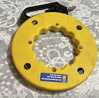 Yellow circular fish tape reel with black handle and label showing product details.