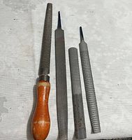 Four assorted metal files including one wooden handled and three metal rasp files on a light surface