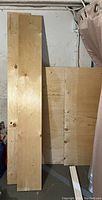 Photo showing three large plywood sheets leaning against a wall, natural wood color with knots and grain visible.