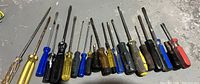 Photo shows twenty assorted screwdrivers with various handle colors and types, several flathead and Phillips types visible.