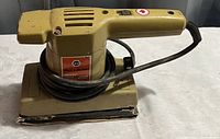 Photo of a vintage Black & Decker electric sander with beige body and rectangular sanding base, cord wrapped around handle.