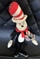 Full view of Cat in the Hat plush toy sitting on black quilted surface with visible original tags attached to arm.