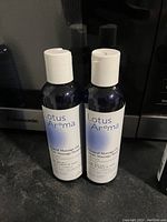 Two unopened dark bottles with white flip-top caps labeled Lotus Aroma natural massage oil.