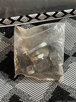 Photo shows new shut off valve in sealed transparent plastic bag on patterned surface.