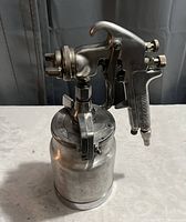 Photo showing one of the stainless steel handheld paint sprayers with attached metal container and adjustment knobs.