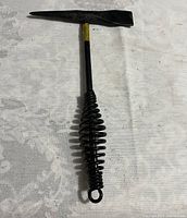 Full view of the black metal straight head clipping hammer with coiled spring handle and yellow marking near the top, placed on a white surface.