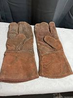 Photo showing a pair of brown suede leather welding gloves placed flat on a surface with fingers and thumbs visible.