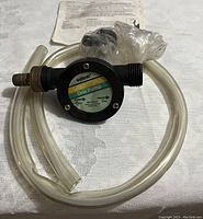 Photo of Wolfcraft self priming drill pump with attached clear tubing and fittings on a fabric surface, showing the pump label and overall assembly.