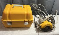 Workforce electric tile cutter saw with water tubing for wet cutting, placed next to the closed yellow hard carrying case.