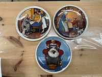 Three circular Norman Rockwell Mother's Day collector plates with illustrations, displayed on wooden surface.