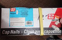 Photo of the closed white and blue box labeled Grip Rite Plastic Cap Nails showing product details, quantity, and branding.
