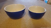 Two nested ceramic mixing bowls, showing the larger and smaller sizes side by side on carpeted floor.