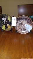 Two W S George collector plates displayed on stands, one depicting a panda and the other a snow leopard.