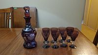 Photo of entire set on a wood table showing one decanter and eight purple crystal glasses.