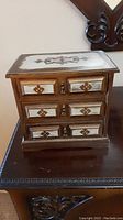 Front view of the wooden jewelry box showing three drawers with decorative inlays and metal pulls.