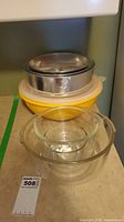 Side view showing one yellow plastic mixing bowl, white plastic lid, metal springform pan, and three clear glass mixing bowls nested.