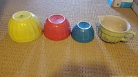 Photo showing three colorful nesting mixing bowls and one green bowl with spout and handle lined up on carpet.