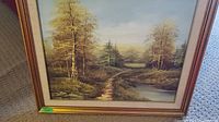 Framed painting showing a forest stream landscape with trees and a small water channel.