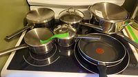 Overall view of multiple Lagostina stainless steel pots and two non-stick frying pans on stove