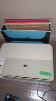 Closed HP Photosmart C4580 printer with filing box behind and HP ink cartridges at front on floor.