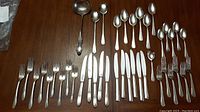 Full view of all silverplate cutlery laid on wooden surface showing various forks, knives, spoons, sugar spoon, salad servers, and soup ladle