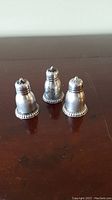 Three silver shakers on a wooden table showing front and size relation.
