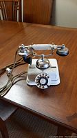 Front view of white vintage style rotary dial table phone with metal bell and fabric cord, placed on a wooden table.