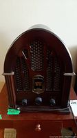 Front view of the antique style AM/FM table radio showing wooden arched cabinet, decorative speaker grille, control knobs and dial window.