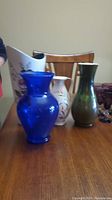 Photo showing four vases: one blue glass, two white ceramic with floral paintings, one green-toned glass.