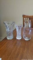 Three vases on wooden table, two cut crystal and one etched glass with floral design, showing entire set