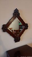Front view of the diamond-shaped wall mirror with carved wood frame and beveled edge glass, reflecting room furniture.