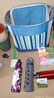 Blue insulated cooler bag with striped pocket, three water bottles, and sandwich kit on floor