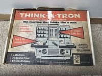Top view of the original box for Think-A-Tron showing the product name, slogan, and images of the machine. The box displays mid-century graphic design and marketing copy highlighting the machine's features.