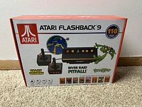 Box of Atari Flashback 9 console with images of joysticks, console, and classic game art on carpet background