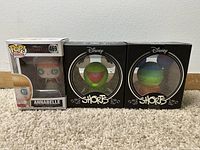 Front view of the Annabelle Funko Pop vinyl figure and two Disney Shorts vinyl figures in black packaging against a plain wall.