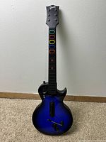 Front view of the Guitar Hero Les Paul wireless controller in blue sunburst finish with colored fret buttons and detailed guitar shape.
