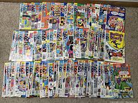 Wide view of multiple Archie Comics arranged in rows on carpet, showing a variety of series and issue covers.