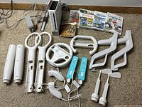 Full lot of Nintendo Wii console, remotes, accessory attachments, and game cases displayed on carpeted floor