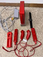 Top-down view of the red Nintendo Wii console, red Wii Remote, Nunchuk, Classic Controller, silicone sleeve, and power cable arranged on the floor.
