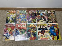 Top view photo showing 11 Marvel comic books laid out on carpet, each in a protective sleeve. Titles include Infinity War, Warlock and the Infinity Watch, She-Hulk, Superboy, Sub-Mariner, Fantastic Four, ROM, X-Factor, and Spider-Man.