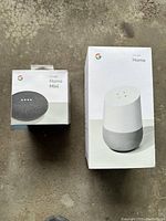 Photo showing front of sealed boxes of Google Home and Google Home Mini on the floor.