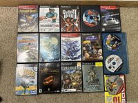 Photo showing 14 different PlayStation 2 game cases arranged on a carpet, featuring titles such as Madden 06, Guitar Hero II, Call of Duty, and Kingdom Hearts series.