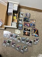 A large box and two trays filled with hundreds of Star Trek trading cards, along with numerous loose cards spread on the floor including boxed packs, character cards, and collectible cards.